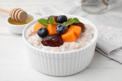 Photo of Delicious barley porridge with blueberries, pumpkin, dates and mint in bowl on white table, closeup