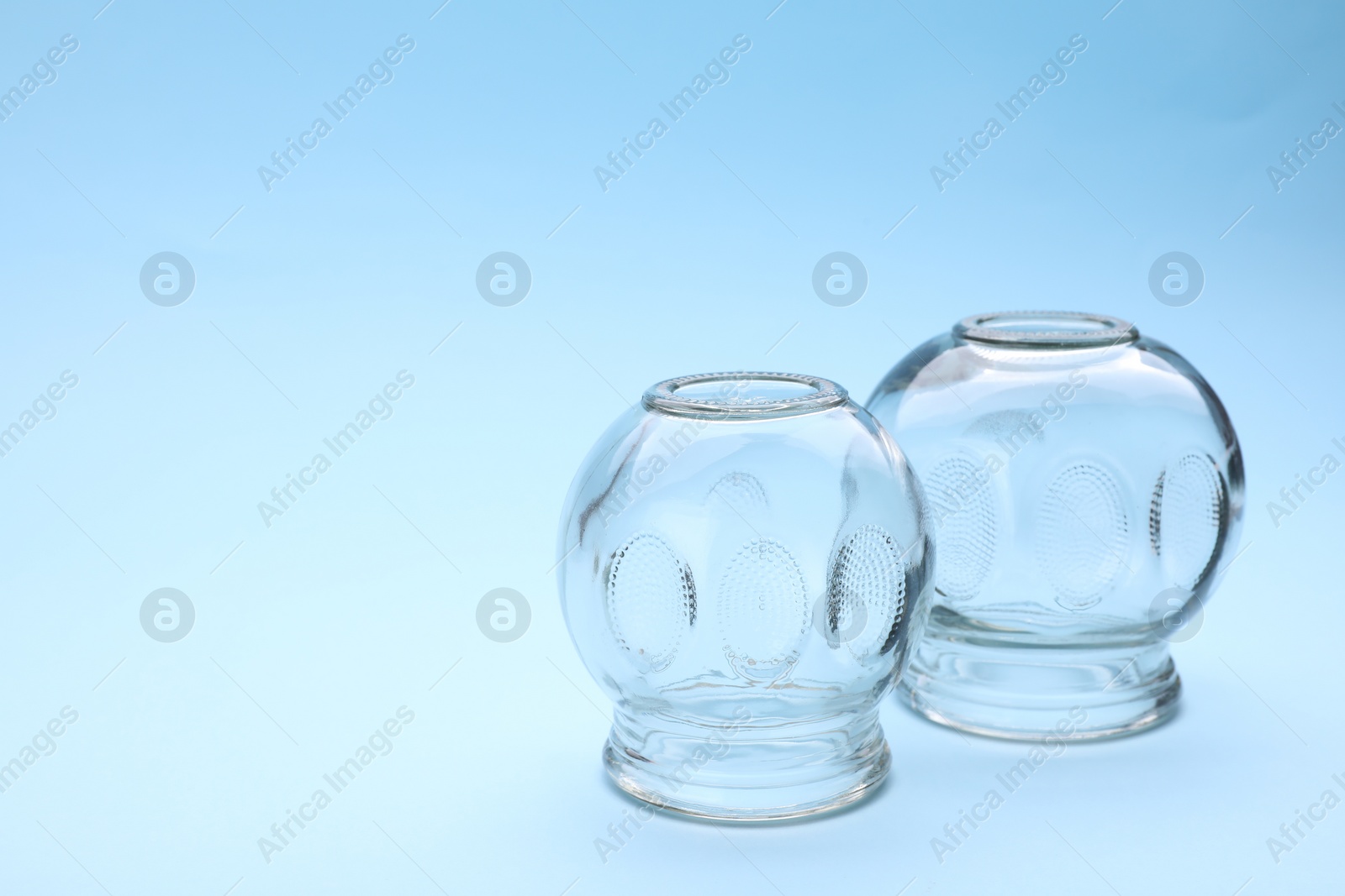 Photo of Glass cups on light blue background, space for text. Cupping therapy