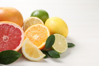 Photo of Different cut and whole citrus fruits on white wooden table, closeup. Space for text