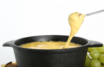 Dipping piece of bread into fondue pot with tasty melted cheese isolated on white