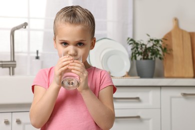 Cute little girl drinking fresh water from glass in kitchen