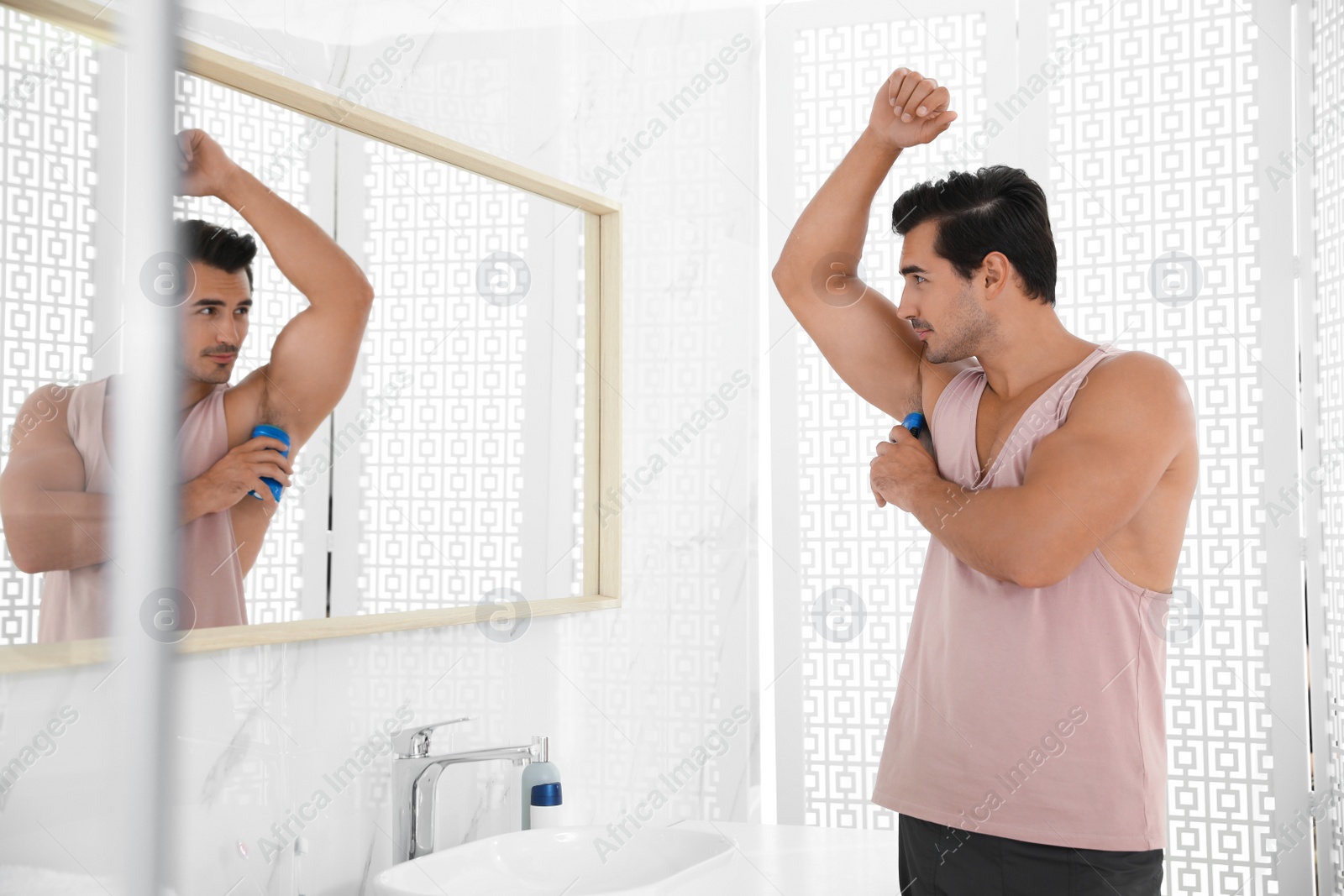 Photo of Handsome young man applying deodorant in bathroom