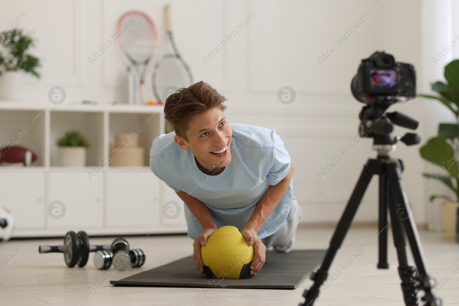 Photo of Smiling sports blogger training with medicine ball while recording fitness lesson with camera at home