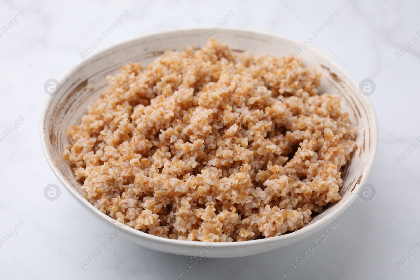 Photo of Tasty wheat porridge in bowl on white marble table, closeup