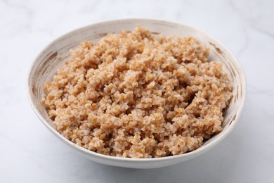 Photo of Tasty wheat porridge in bowl on white marble table, closeup