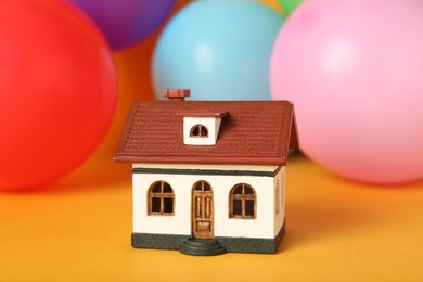 Photo of House model and balloons on yellow background. Housewarming party