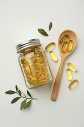 Bottle, vitamin capsules, spoon and leaves on white background, flat lay