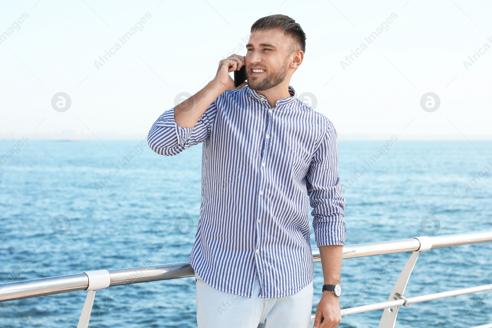 Photo of Portrait of handsome young man talking on phone near sea