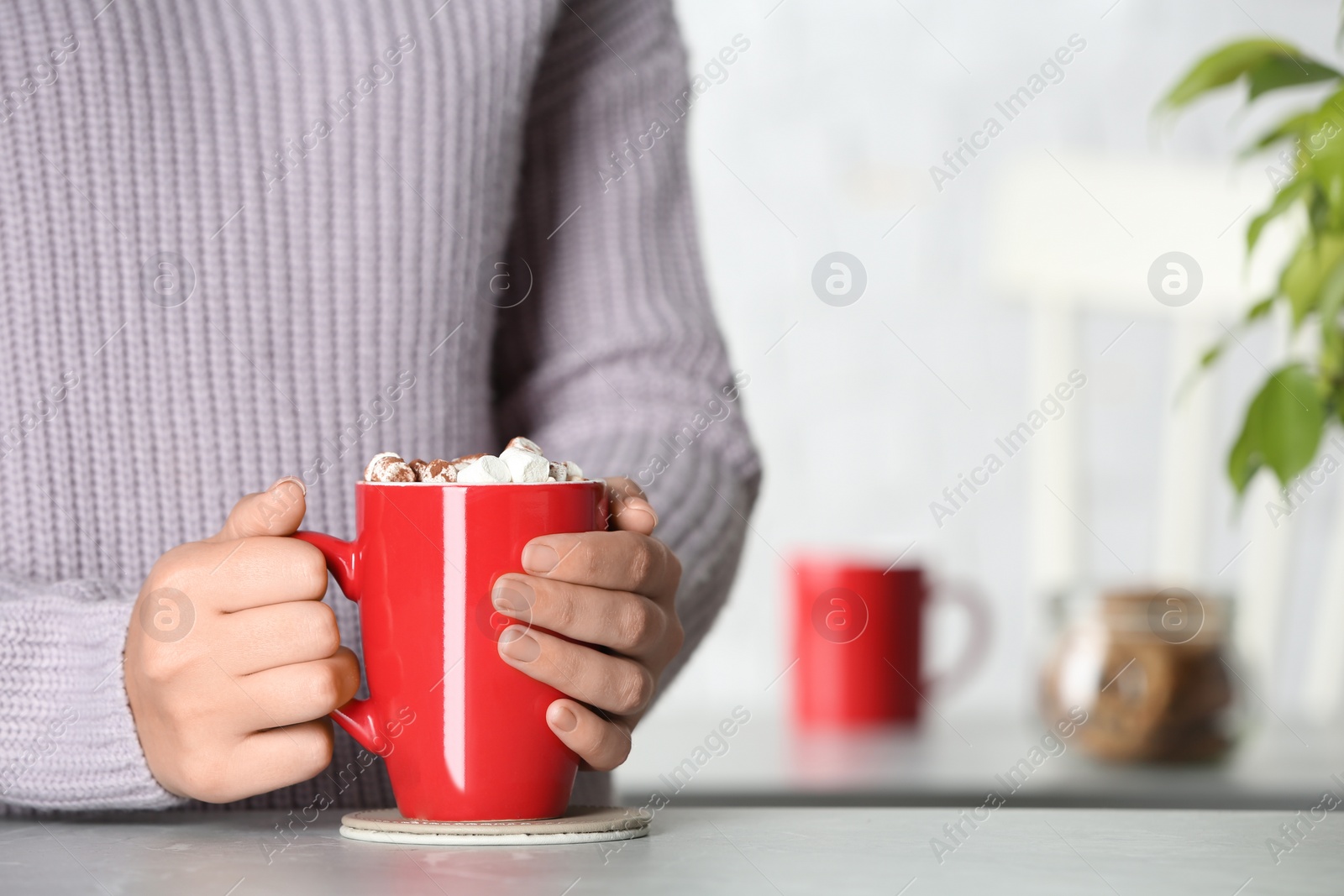 Photo of Woman holding cup of tasty cocoa with marshmallows at table indoors, closeup. Space for text