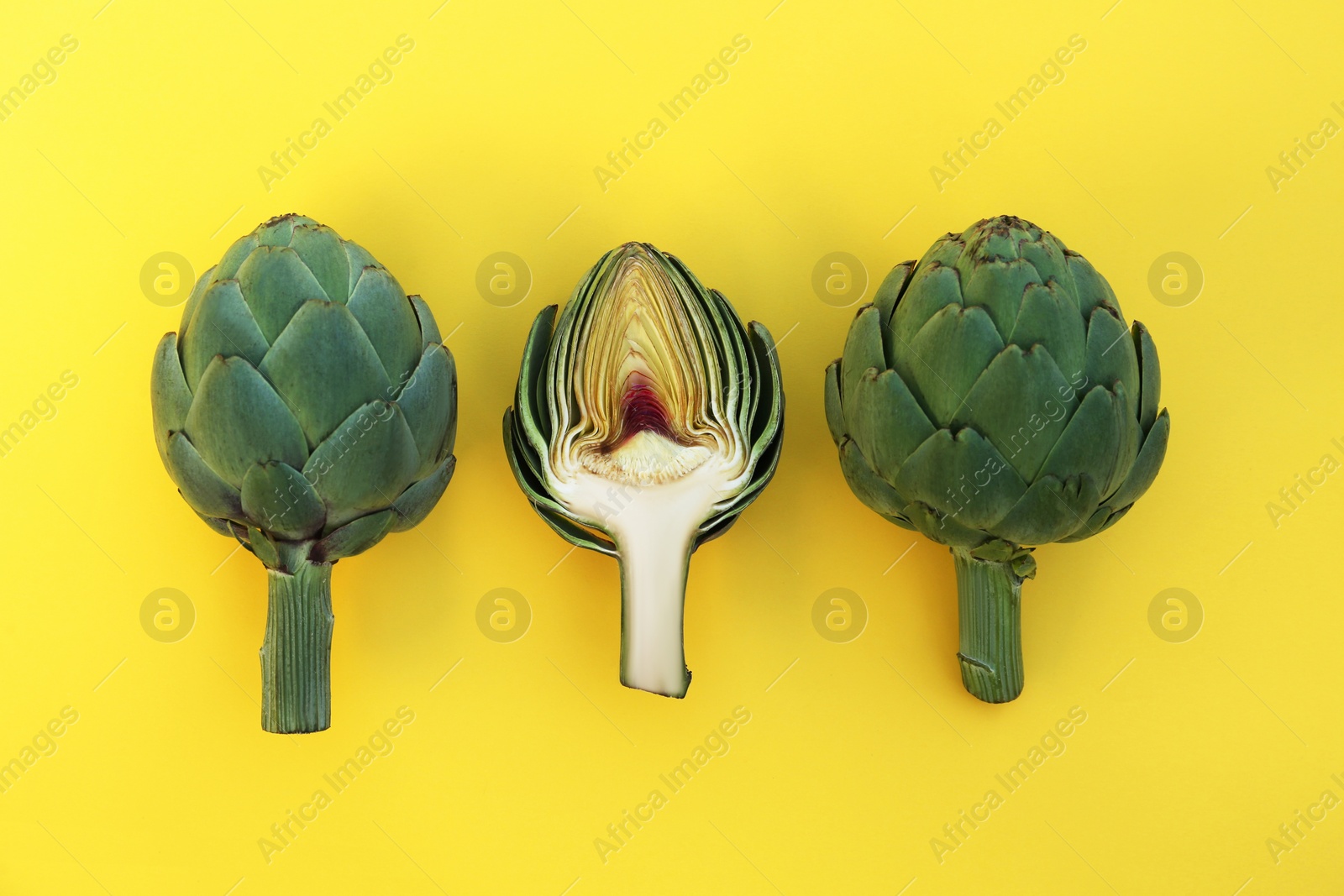 Photo of Cut and whole fresh raw artichokes on yellow background, flat lay