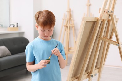 Photo of Little boy painting in studio. Using easel to hold canvas