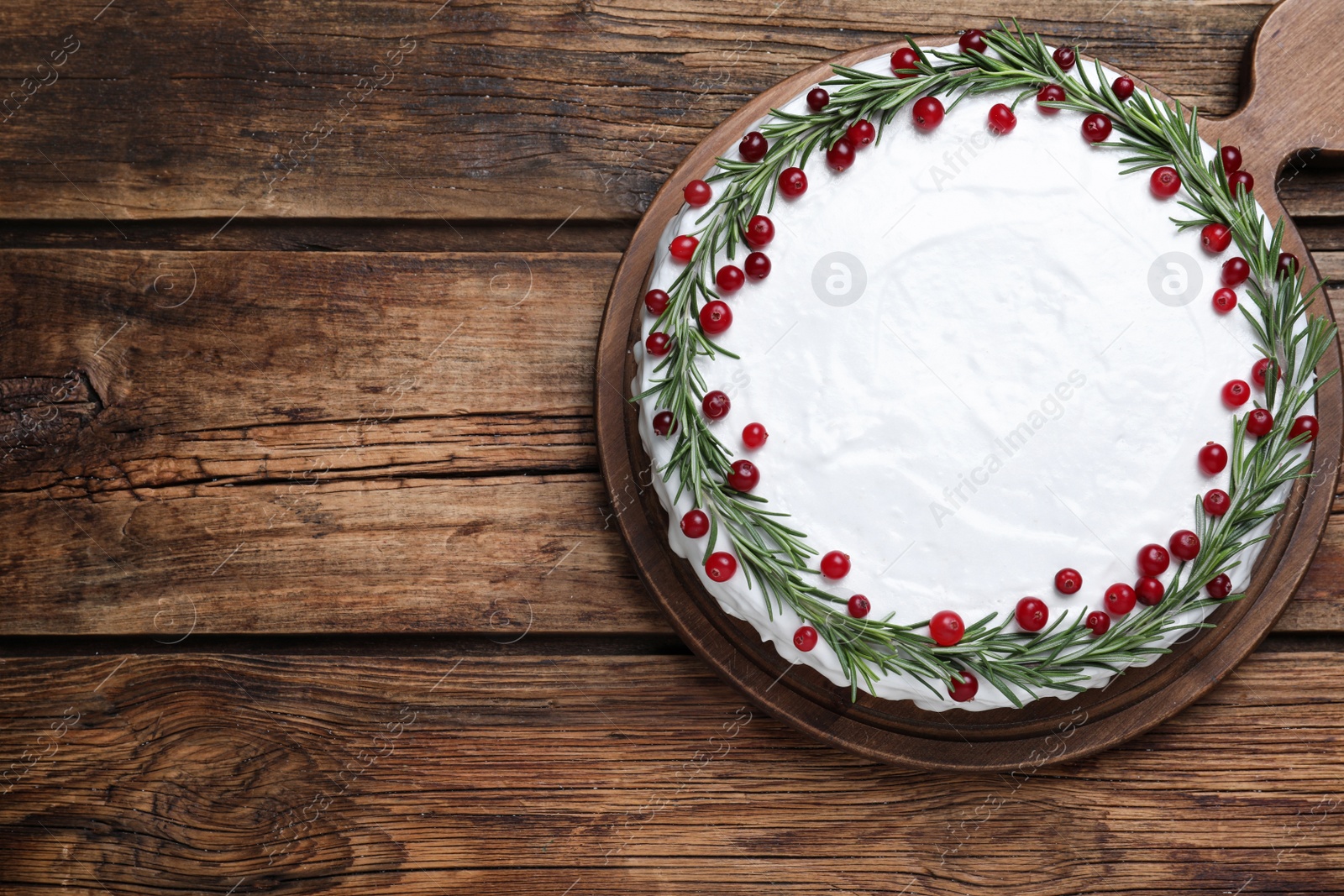Photo of Traditional Christmas cake decorated with rosemary and cranberries on wooden table, top view. Space for text