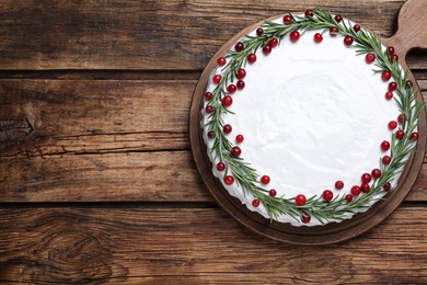 Traditional Christmas cake decorated with rosemary and cranberries on wooden table, top view. Space for text