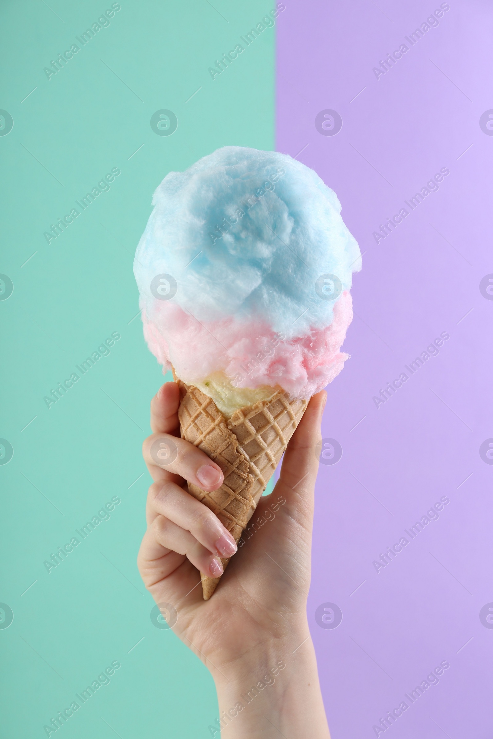 Photo of Woman holding waffle cone with cotton candy on color background, closeup