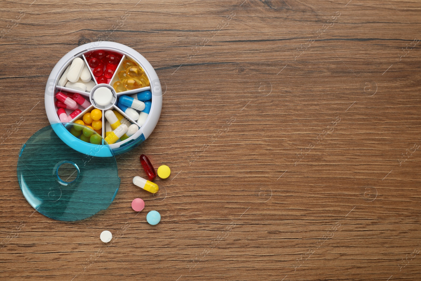 Photo of Plastic box with different pills on wooden table, flat lay. Space for text