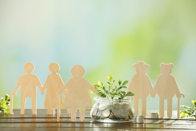 Photo of Pension savings. Figures of elderly people, coins and green twig in jar on blurred background