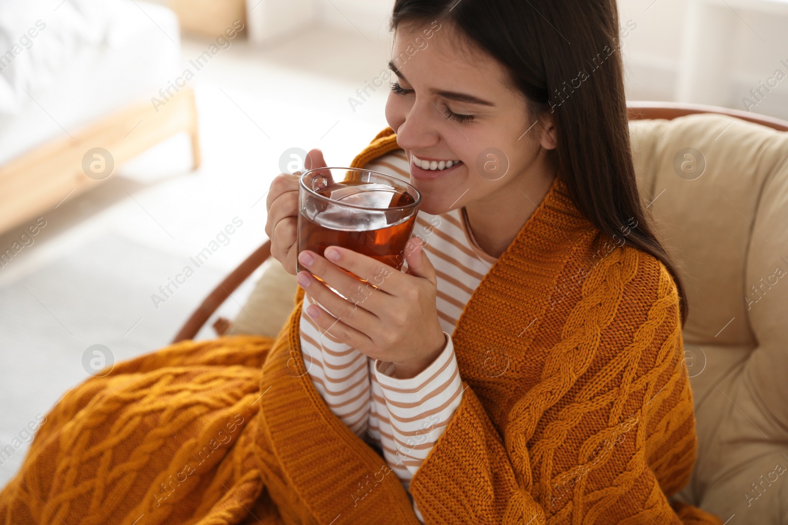 Photo of Woman covered with warm orange plaid enjoying hot drink at home