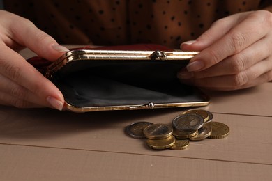 Photo of Poverty. Woman with empty wallet and coins at wooden table, closeup