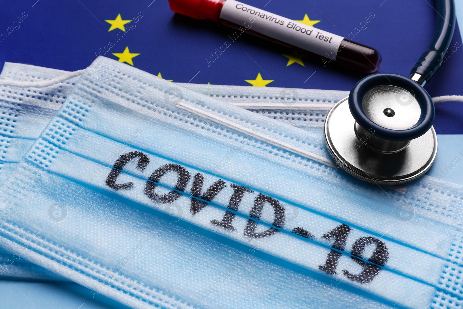 Photo of Protective masks, stethoscope and test tube with blood sample on European Union flag background, closeup. Coronavirus outbreak
