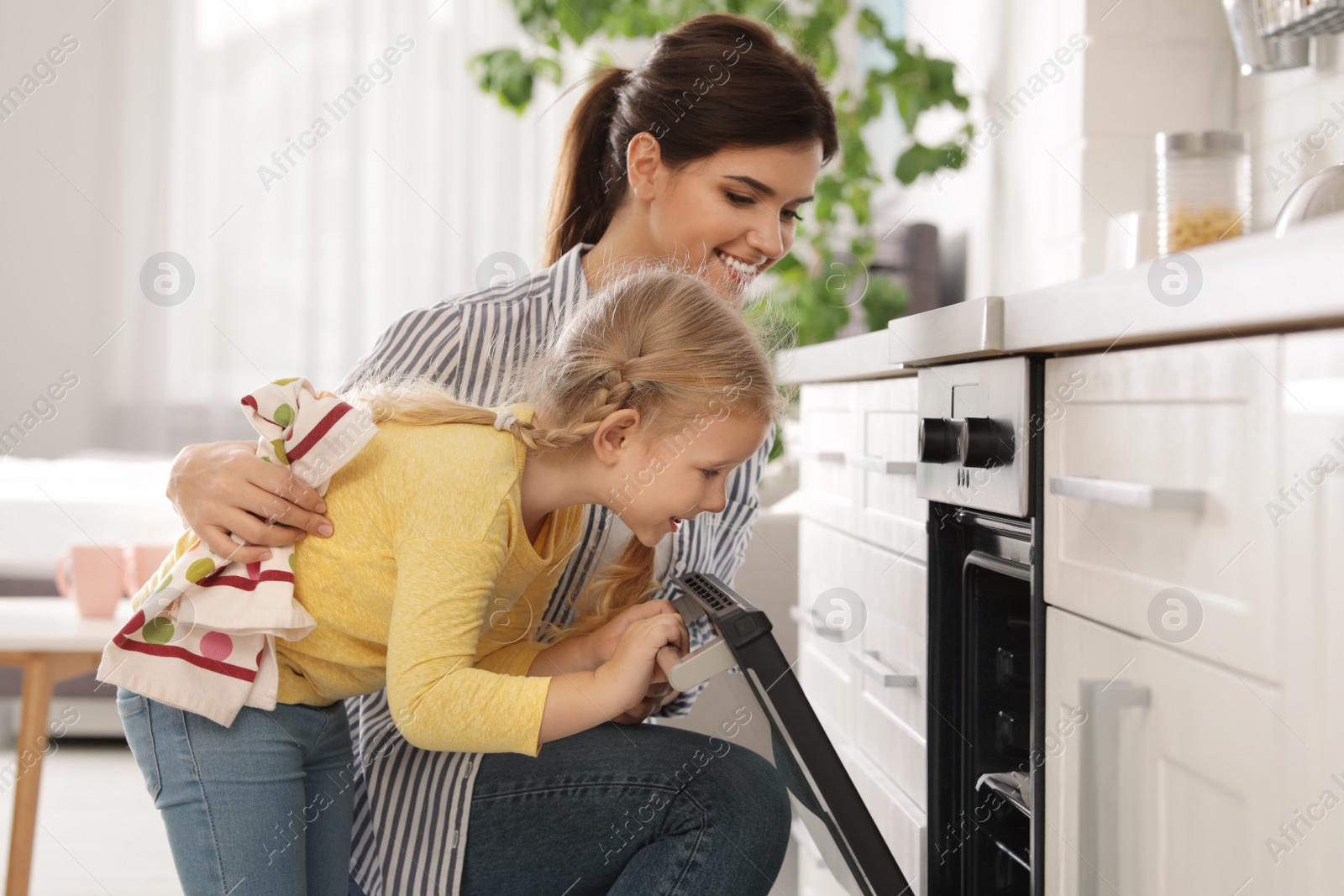 Photo of Mother and daughter opening oven while baking in kitchen