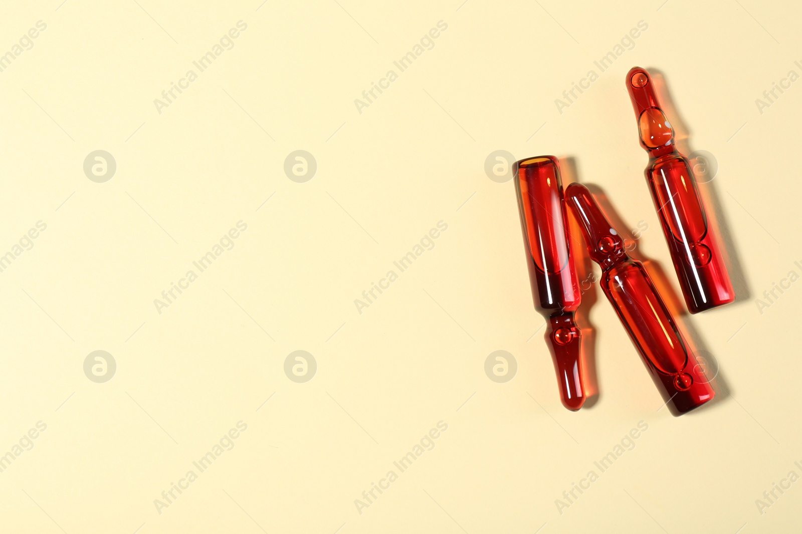 Photo of Glass ampoules with liquid on beige background, top view. Space for text