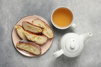Pieces of delicious yeast dough cake and tea on light gray table, flat lay