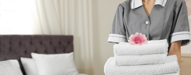 Image of Chambermaid holding stack of fresh towels in hotel room, closeup view with space for text. Banner design