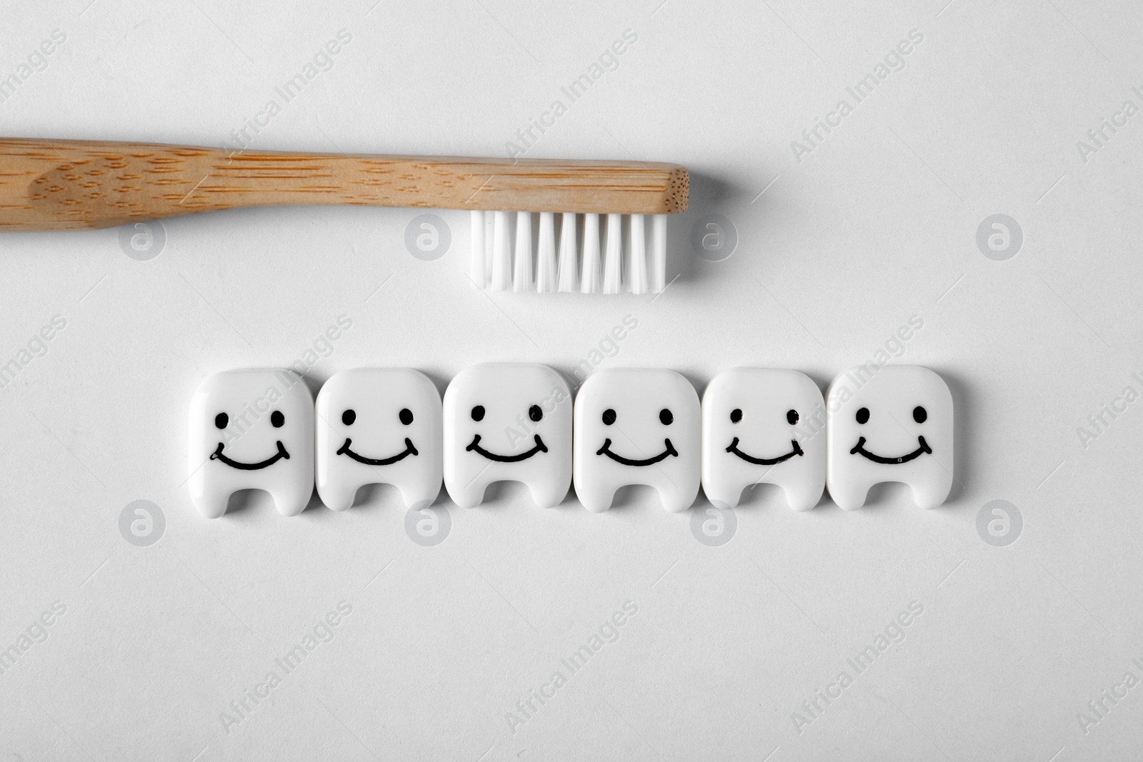 Photo of Small plastic teeth with happy faces and wooden brush on white background, top view