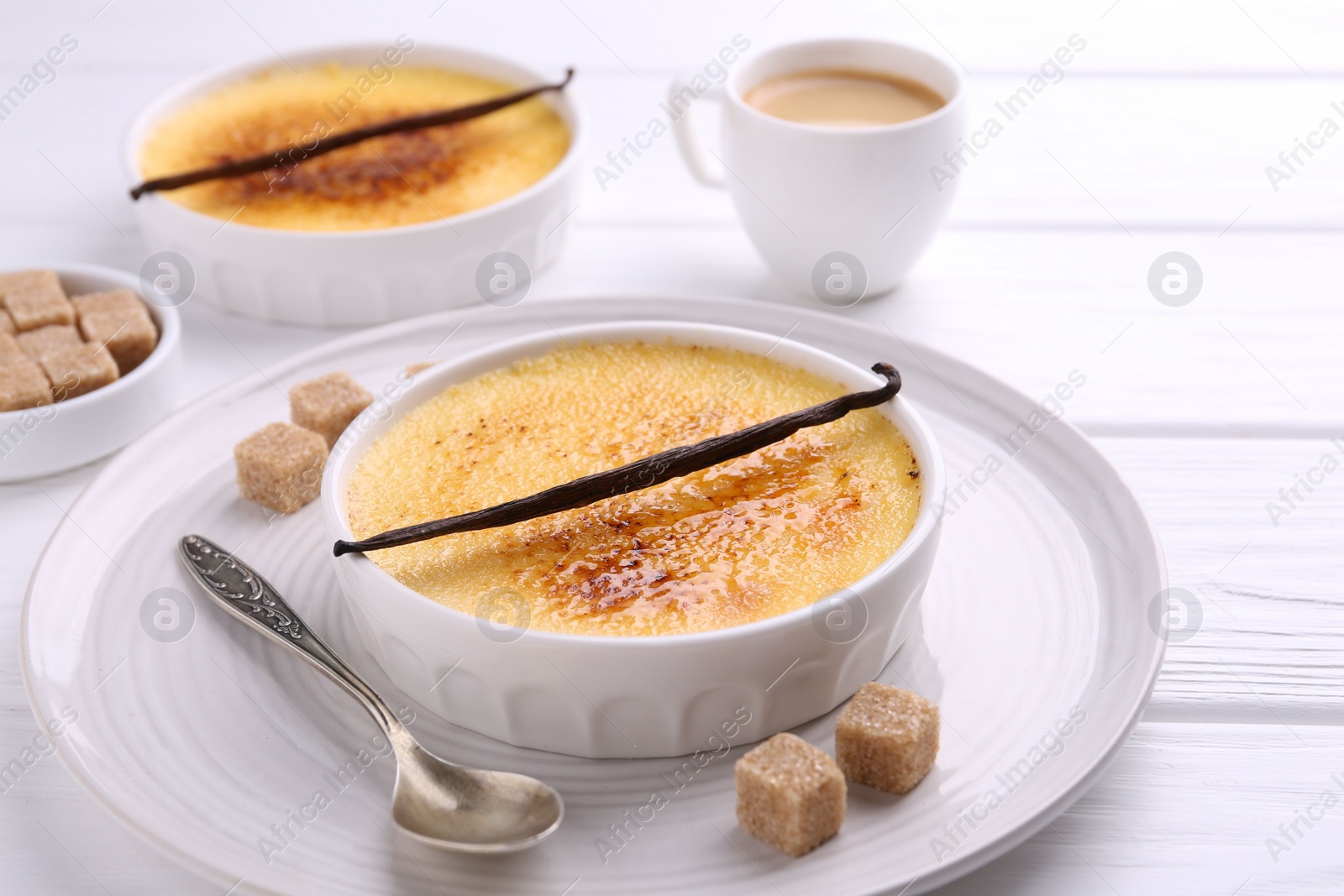 Photo of Delicious creme brulee in bowls, vanilla pods, sugar cubes and coffee on white wooden table