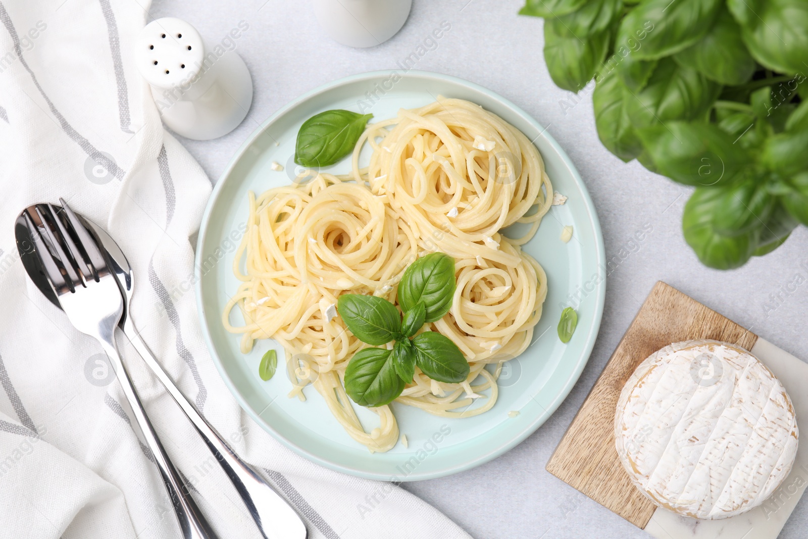 Photo of Delicious pasta with brie cheese and basil leaves served on light grey table, flat lay
