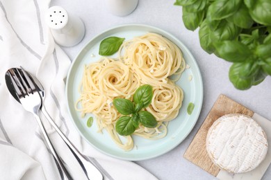 Delicious pasta with brie cheese and basil leaves served on light grey table, flat lay