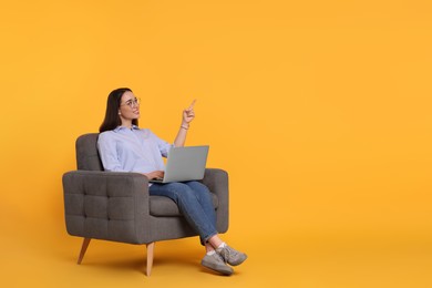 Photo of Smiling young woman with laptop sitting in armchair on yellow background, space for text