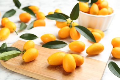 Photo of Fresh ripe kumquats and leaves on wooden board