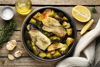 Photo of Pieces of delicious baked cod with vegetables, lemon and spices in dish on wooden table, flat lay