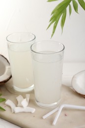 Glasses of coconut water, palm leaves and nuts on white table