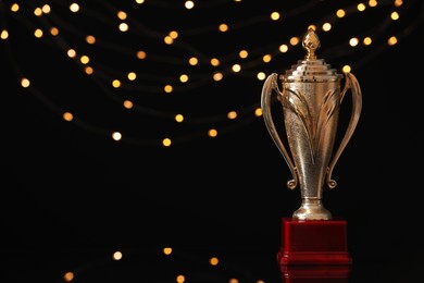 Golden trophy cup against blurred festive lights, space for text