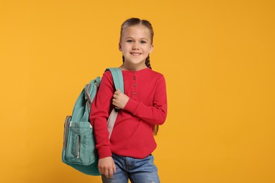 Photo of Happy schoolgirl with backpack on orange background, space for text