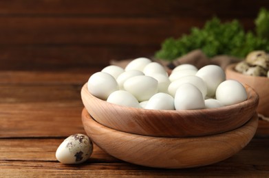 Photo of Many peeled boiled quail eggs and another one in shell on wooden table, closeup