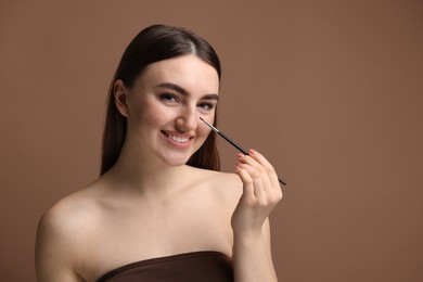 Smiling woman drawing freckles with brush on brown background