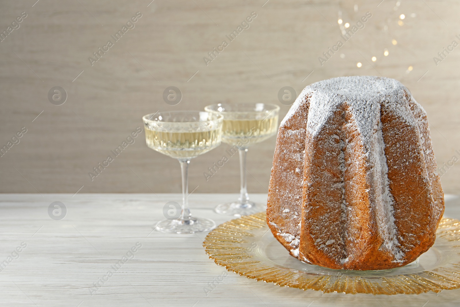 Photo of Delicious Pandoro cake decorated with powdered sugar and sparkling wine on white wooden table, space for text. Traditional Italian pastry
