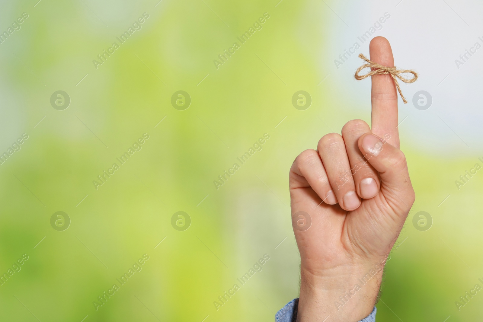 Photo of Man showing index finger with tied bow as reminder on green blurred background, closeup. Space for text