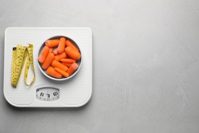 Photo of Healthy diet. Scale with carrots and measuring tape on light grey table, top view. Space for text