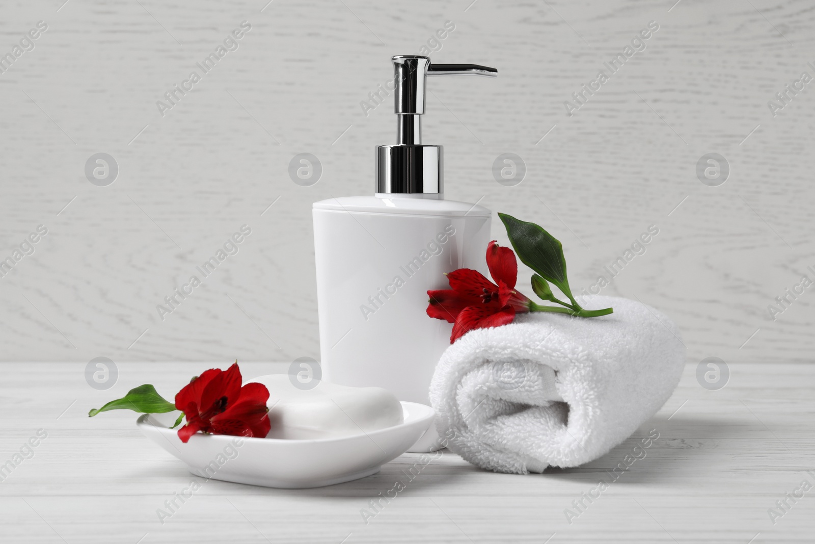 Photo of Dish with soap bar, dispenser and terry towel on white wooden table