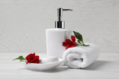 Dish with soap bar, dispenser and terry towel on white wooden table