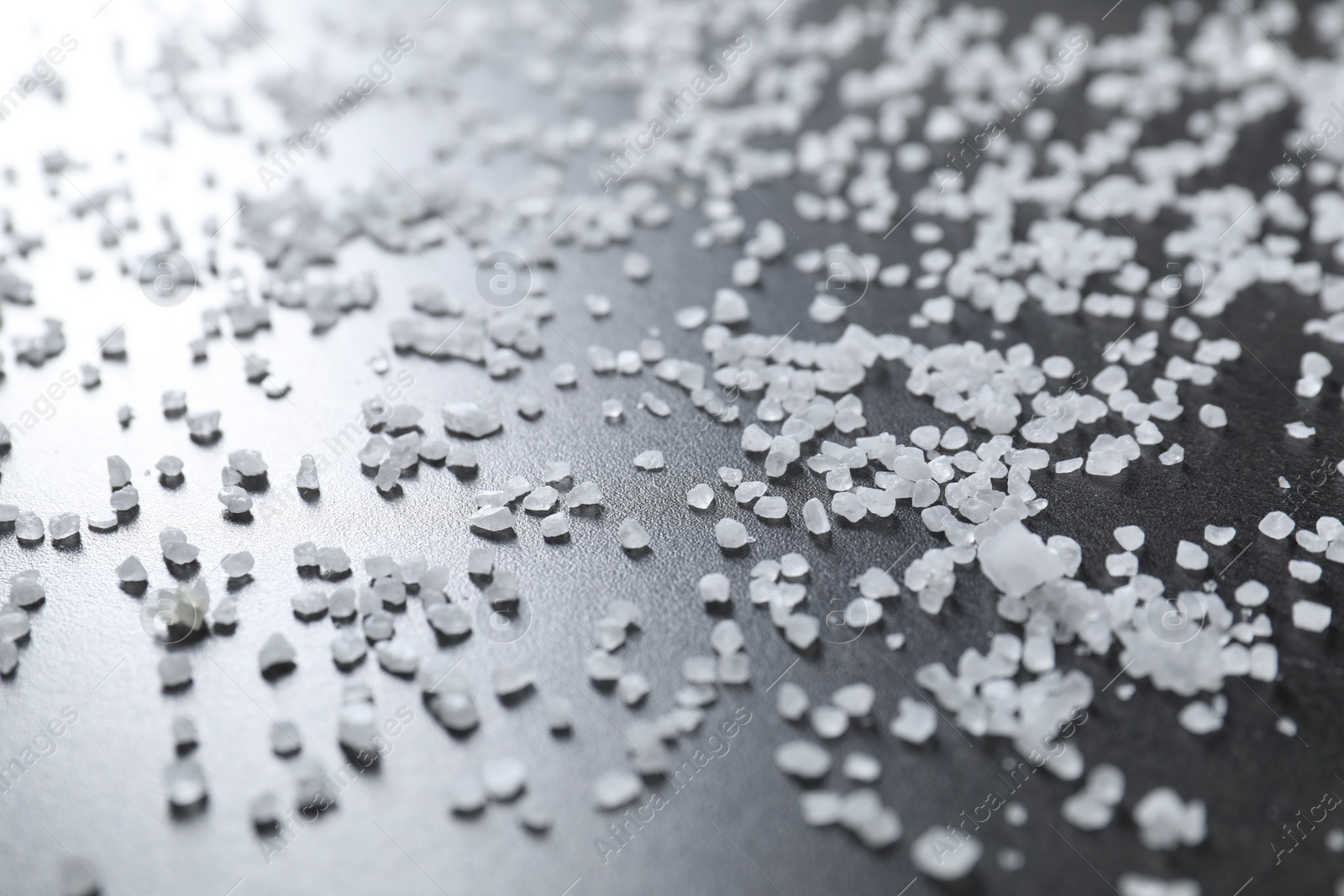 Photo of Scattered white natural salt on black table, closeup