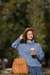 Photo of Young woman with stylish backpack and hot drink on autumn day