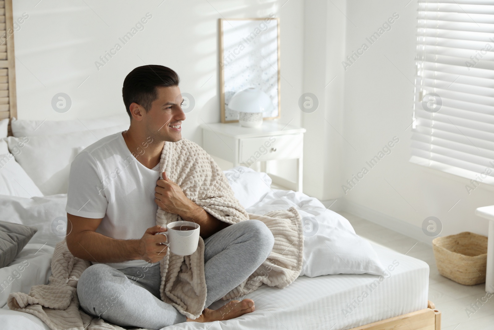 Photo of Man covered with plaid enjoying hot morning drink on bed indoors