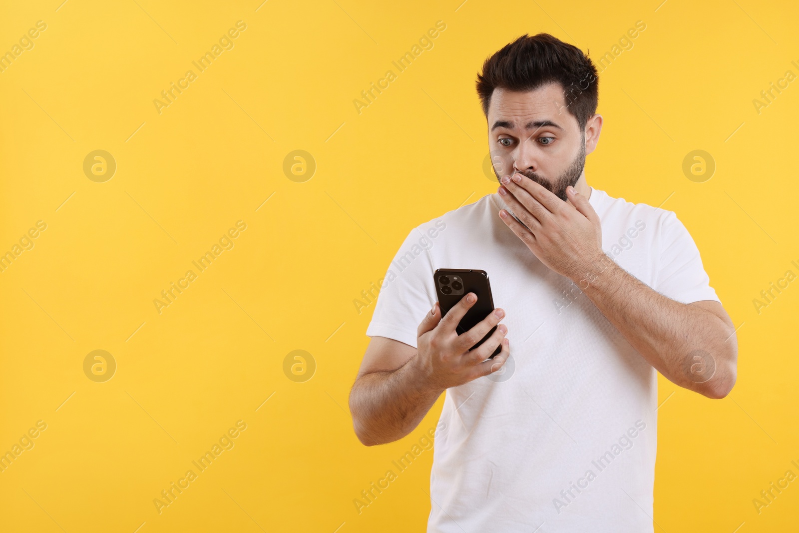 Photo of Shocked young man using smartphone on yellow background, space for text