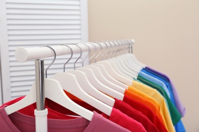 Rack with bright clothes in room. Rainbow colors