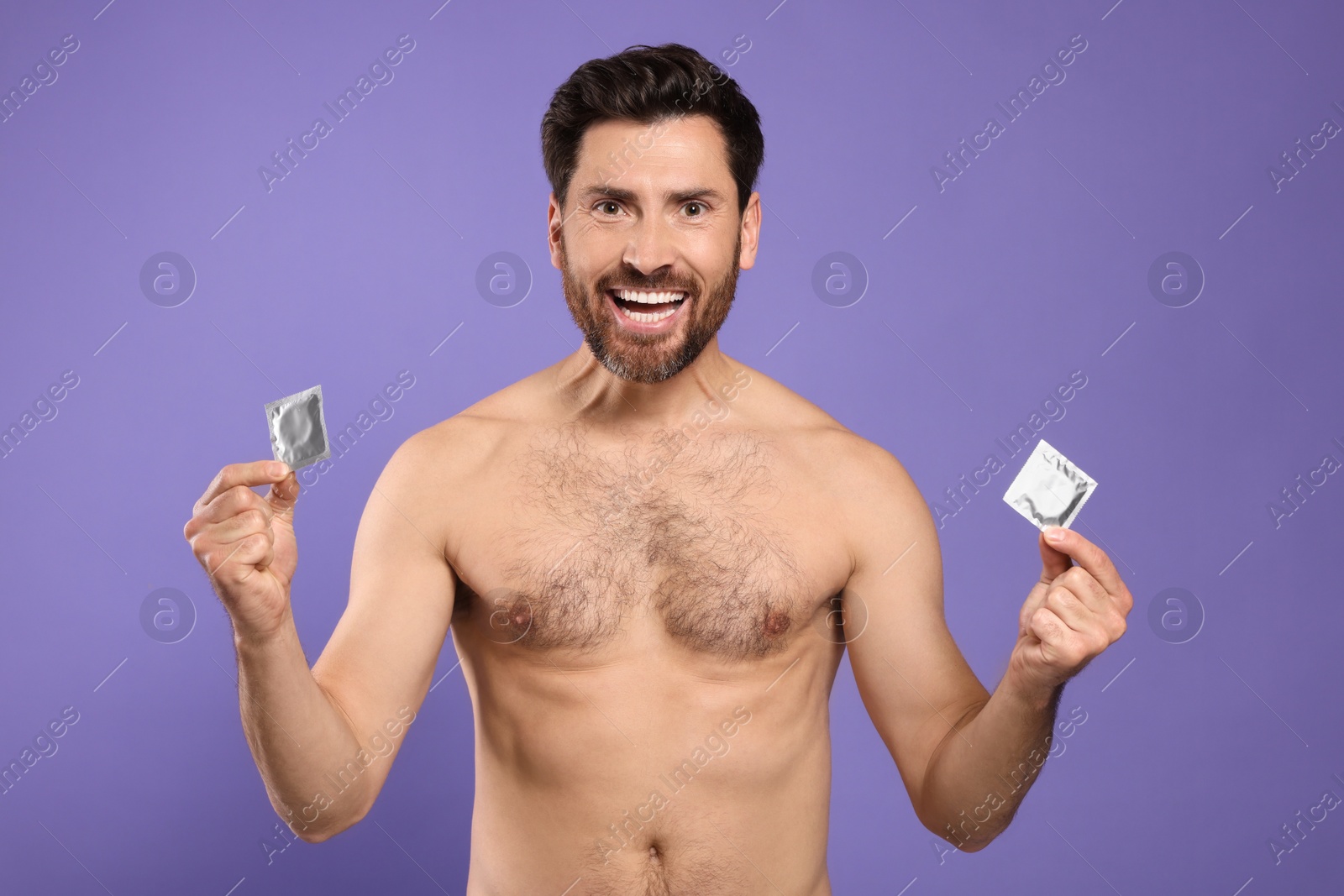 Photo of Emotional naked man holding condoms on purple background. Safe sex